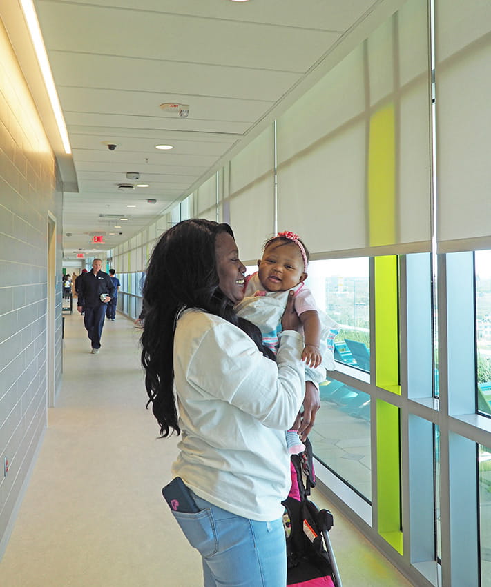 mother holds up her baby in a bright sun-lit hallway and looks outdoors