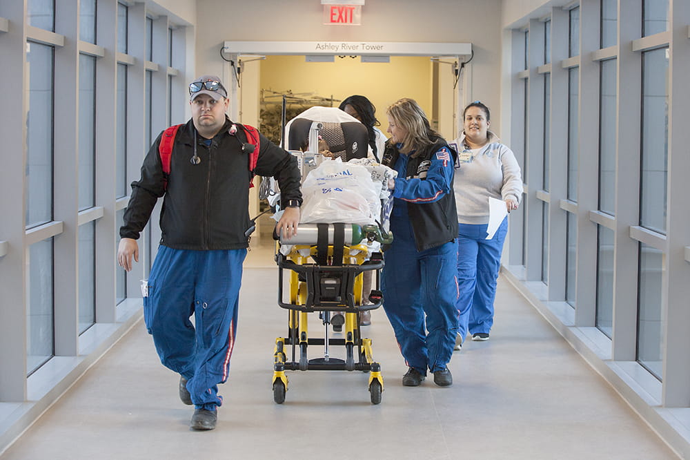 people in flight jumpsuits wheel a large stretcher with a small baby in it