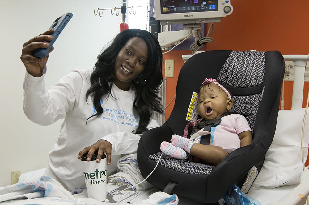 Mya yawns in her car seat atop her baby while mom takes a selfie of the two of them