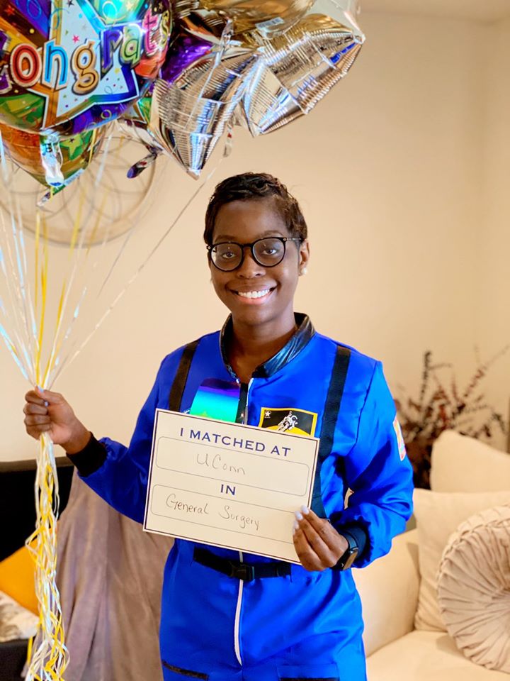 a woman dressed as an astronaut holding balloons and a paper with her match to University of Connecticut
