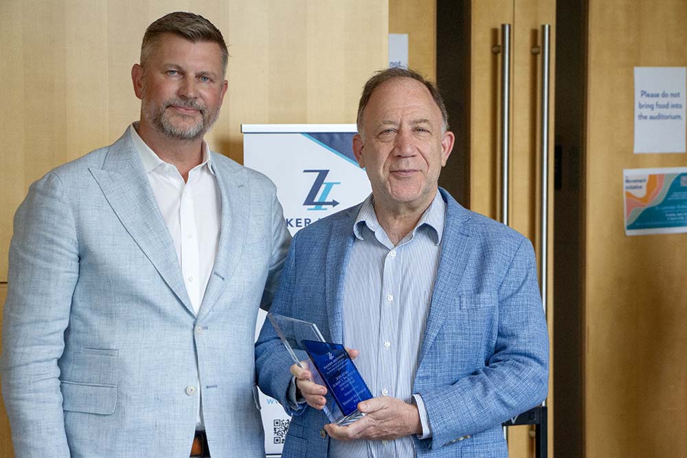Two men in blue sport coats. One is holding a blue award.